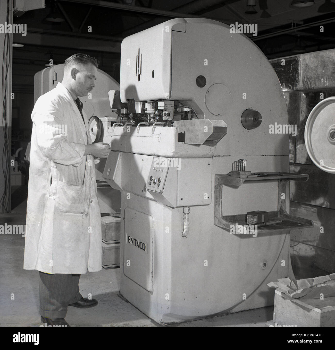 1950s, historical, a white-coated male technican working at a large industrial needle making machine made by Entaco, England, UK. Stock Photo