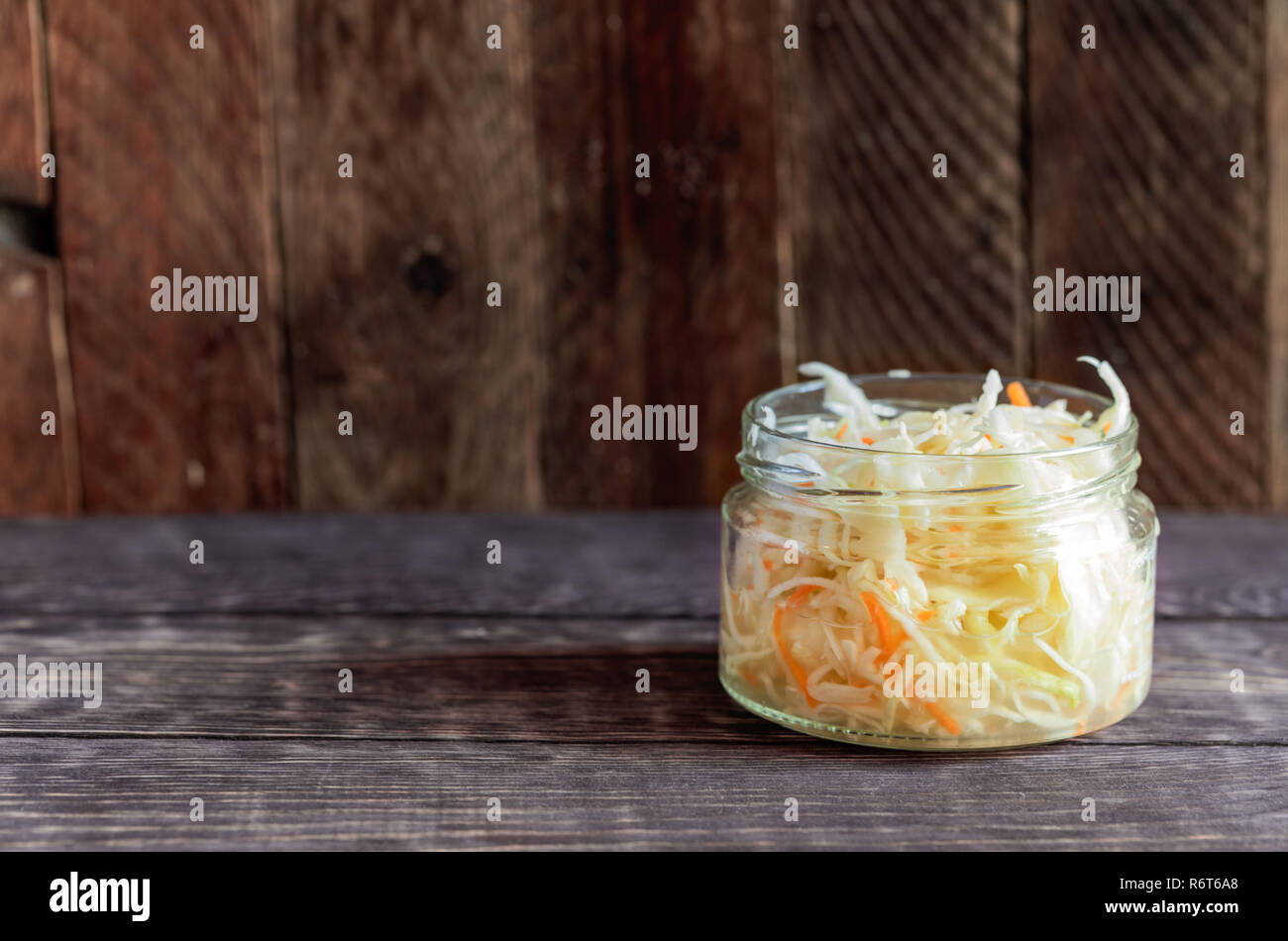 Glass jar with sauerkraut is standing on dark wooden background. Stock Photo