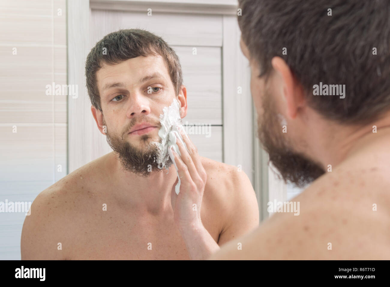 A man is applying shaving foam to his face preparing to shave Stock