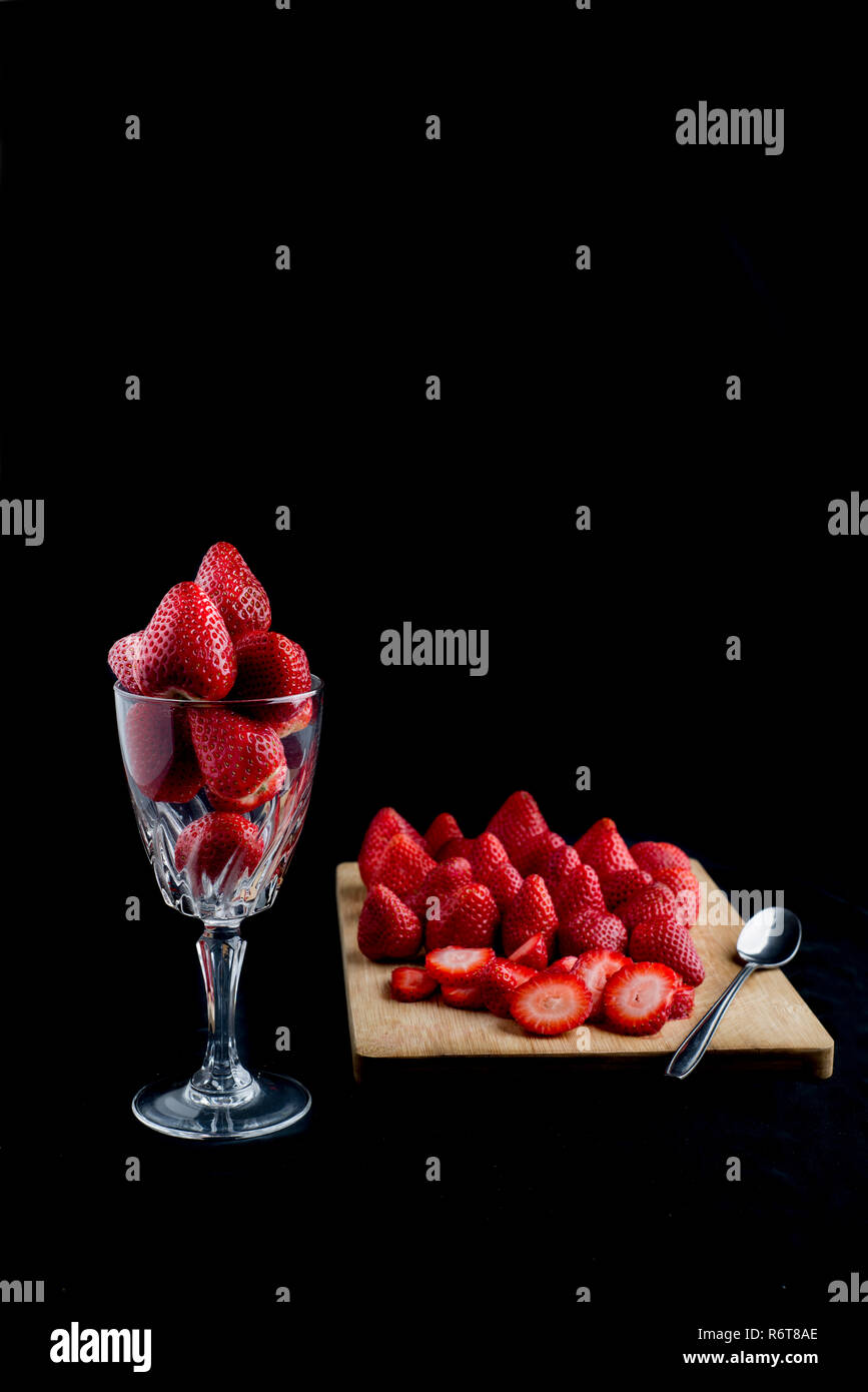 Glass cup full of strawberries beside a cutting board with strawberries and a spoon Stock Photo