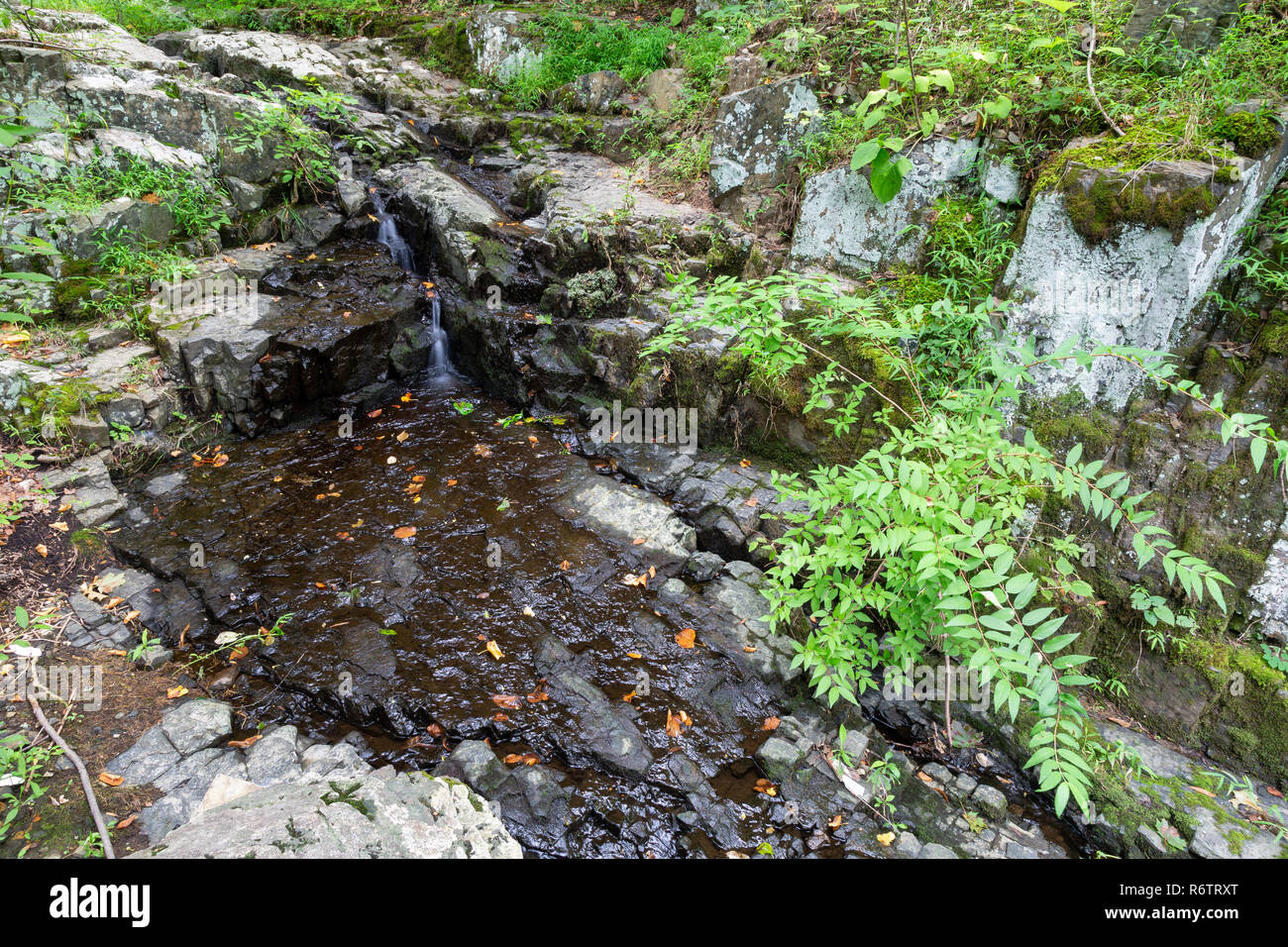 A small trickling cascading waterfall pouring onto geometric rocks