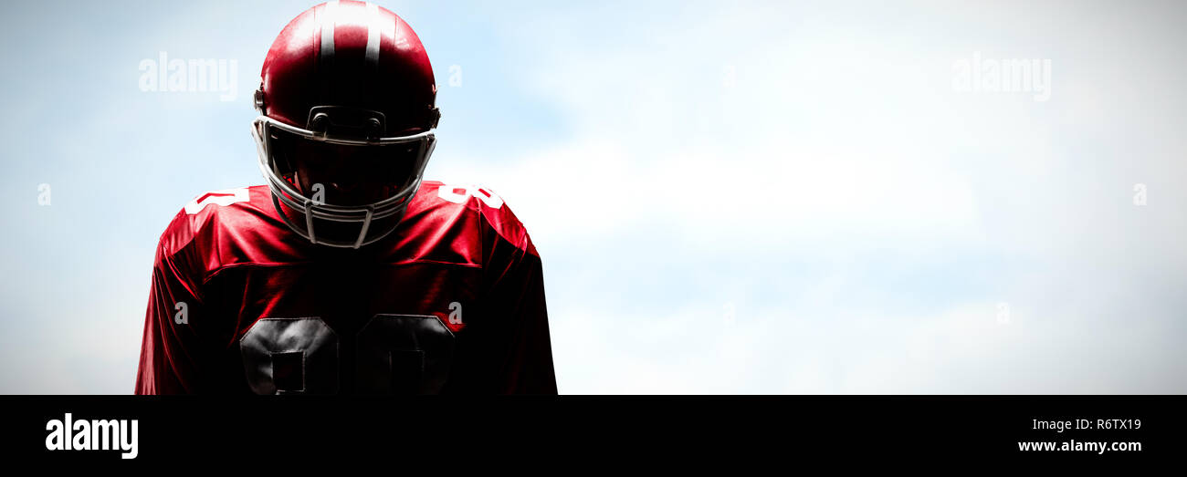 American football player standing in rugby helmet against blue sky with clouds Stock Photo