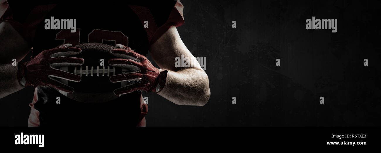 American football player holding rugby ball against full frame shot of grunged concrete wall Stock Photo