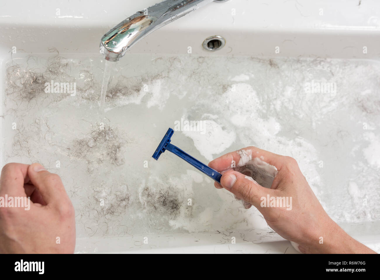 the man is shaving the view of the hands with a razor and the wash basin with dirty water R6W76G