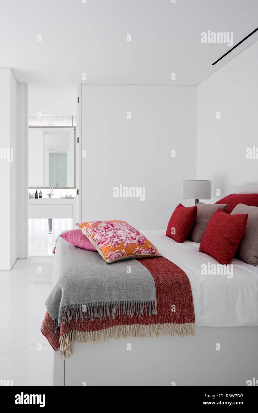 Red and muted pink cushions on double bed with built-in wardrobe in minimalist bedroom of  new build villa, Quinta do Lago Stock Photo