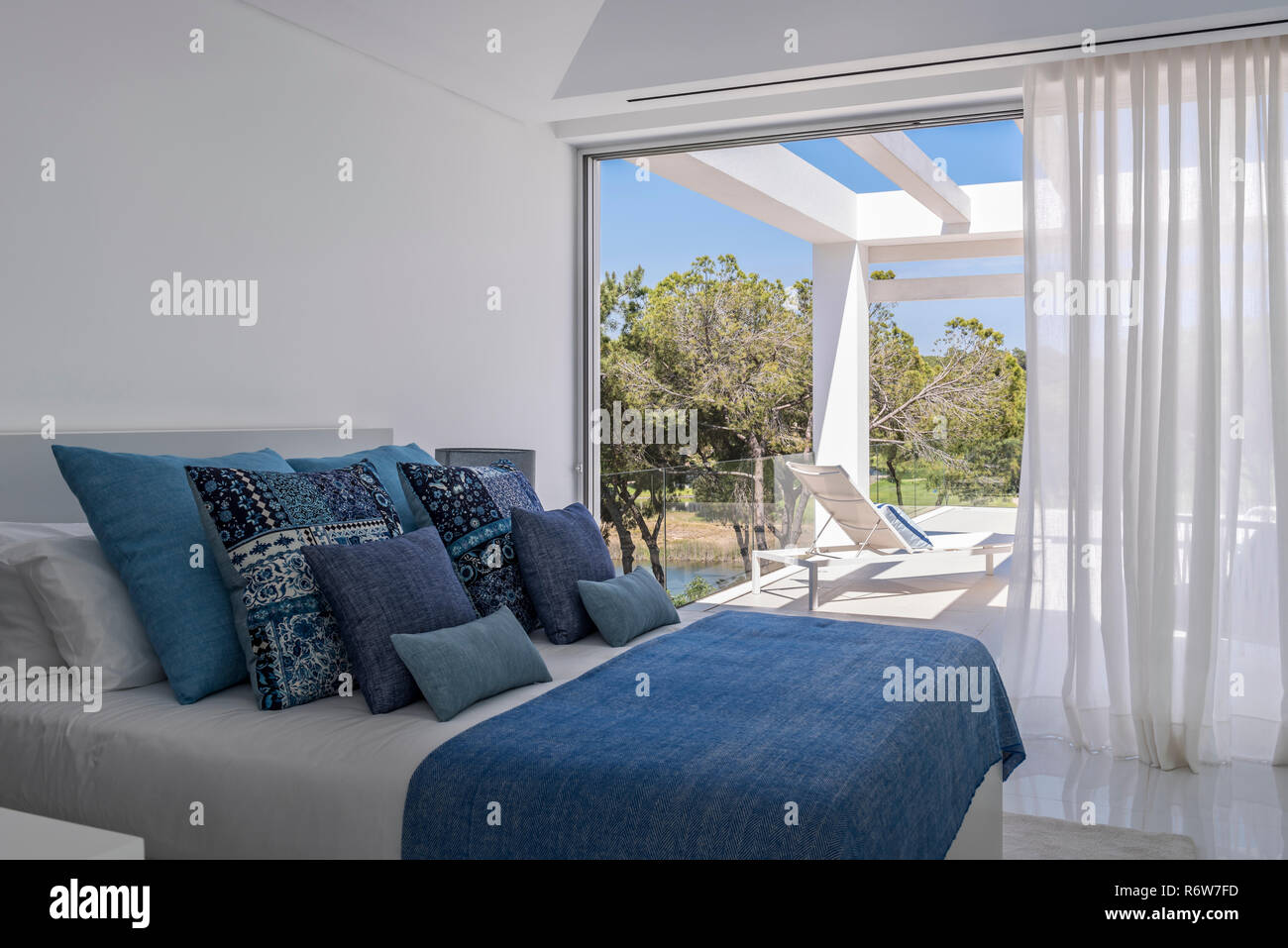 Assorted cushions in hues of blue on double bed with view to poolside terrace in new build villa, Quinta do Lago Stock Photo