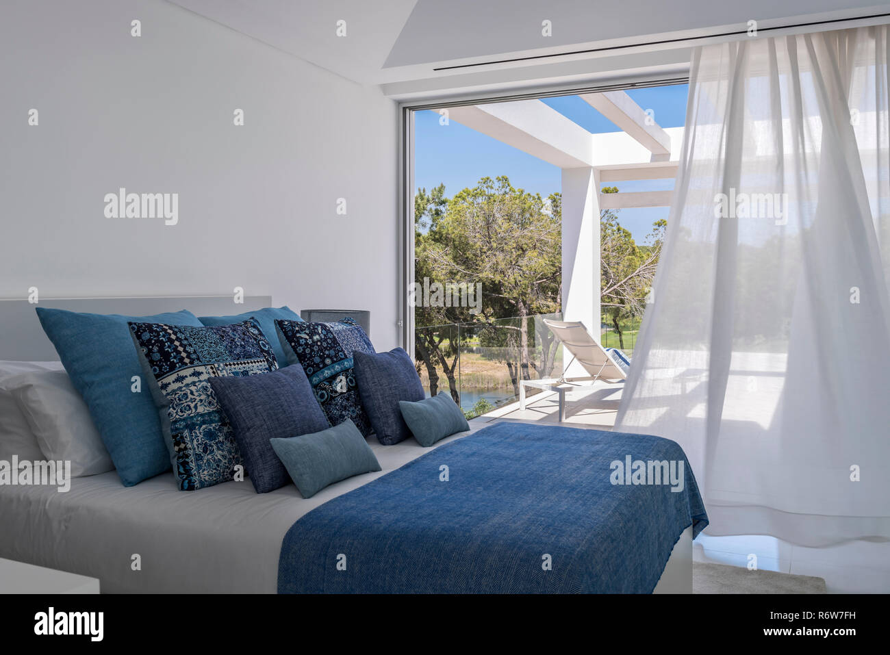 Assorted cushions in hues of blue on double bed with view to poolside terrace in new build villa, Quinta do Lago Stock Photo