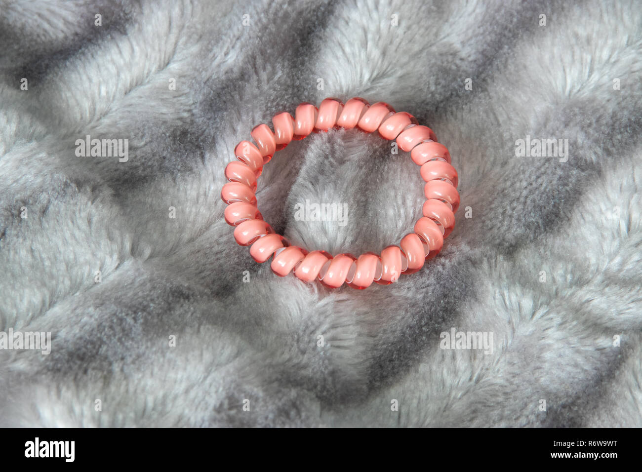 One pink scrunchy hair tie elastic spring on the silver gray fluffy faux fur blanket background Stock Photo