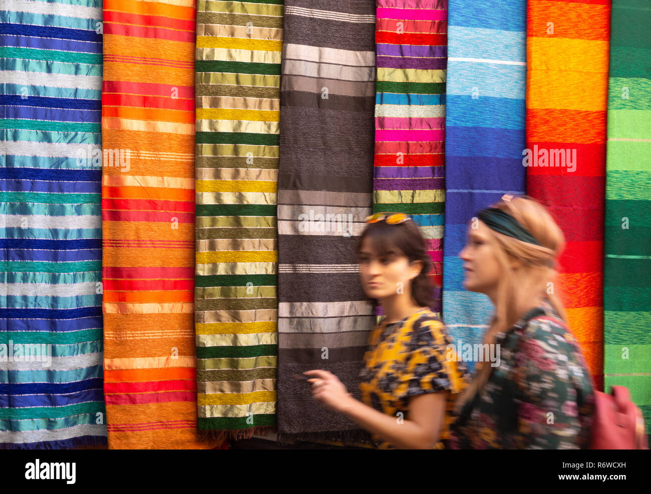 Marrakech tourists - women walking past colourful fabrics in the souk, Marrakech Medina, Marrakesh, Morocco Africa Stock Photo