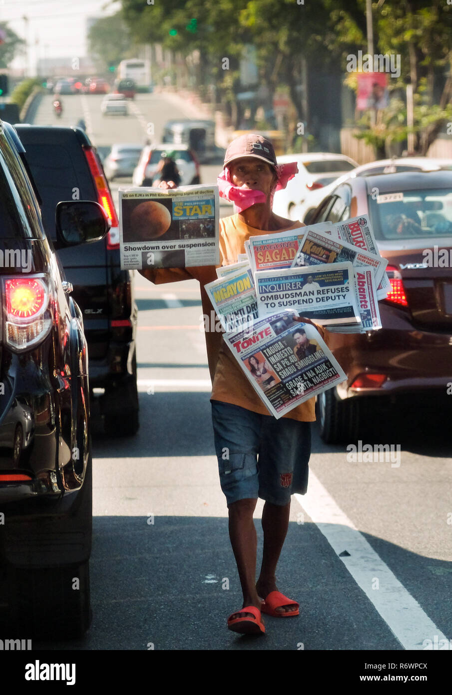 Street vendor between cars in a traffic jam trying to sell newspaper to drivers and passengers in Quezon City, Metro Manila, Philippines Stock Photo