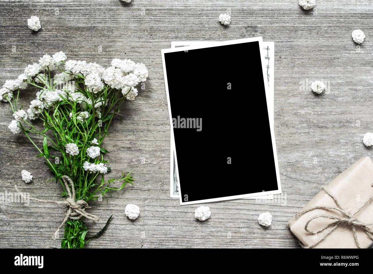 blank photo frame with white flowers bouquet and gift box to put your picture on rustic wooden background .top view. mock up. flat lay Stock Photo