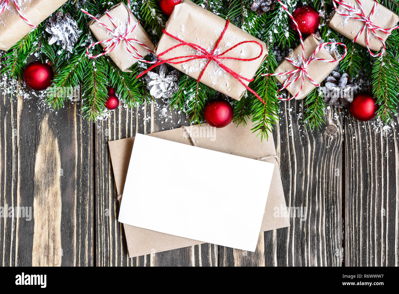 blank christmas greeting card and envelope with fir tree branches, gift boxes, decorations and pine cones on dark wooden background. mock up. top view Stock Photo