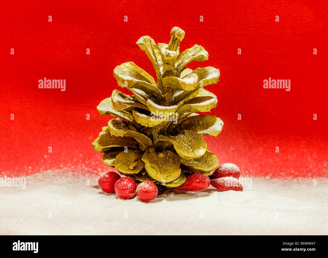 Golden cone and mistletoe covered with snow on red background, close up Stock Photo