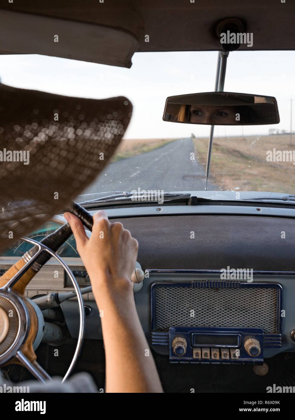 young girl driving a retro car and looks in the rearview mirror Stock