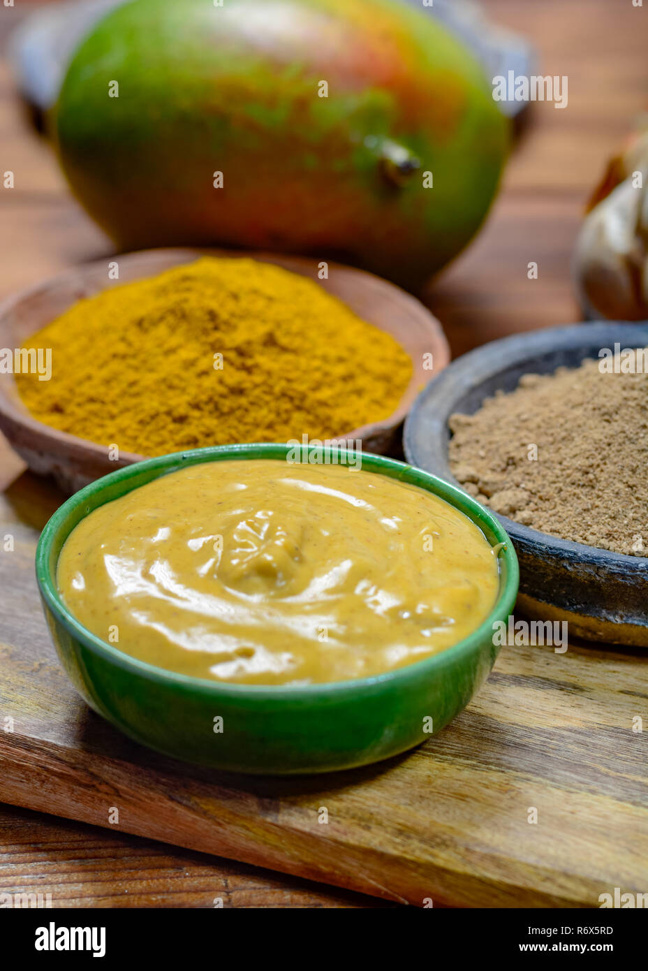 Tasty mango-curry sauce in small bowl ready to eat and bowls with mango and curry powder close- up Stock Photo