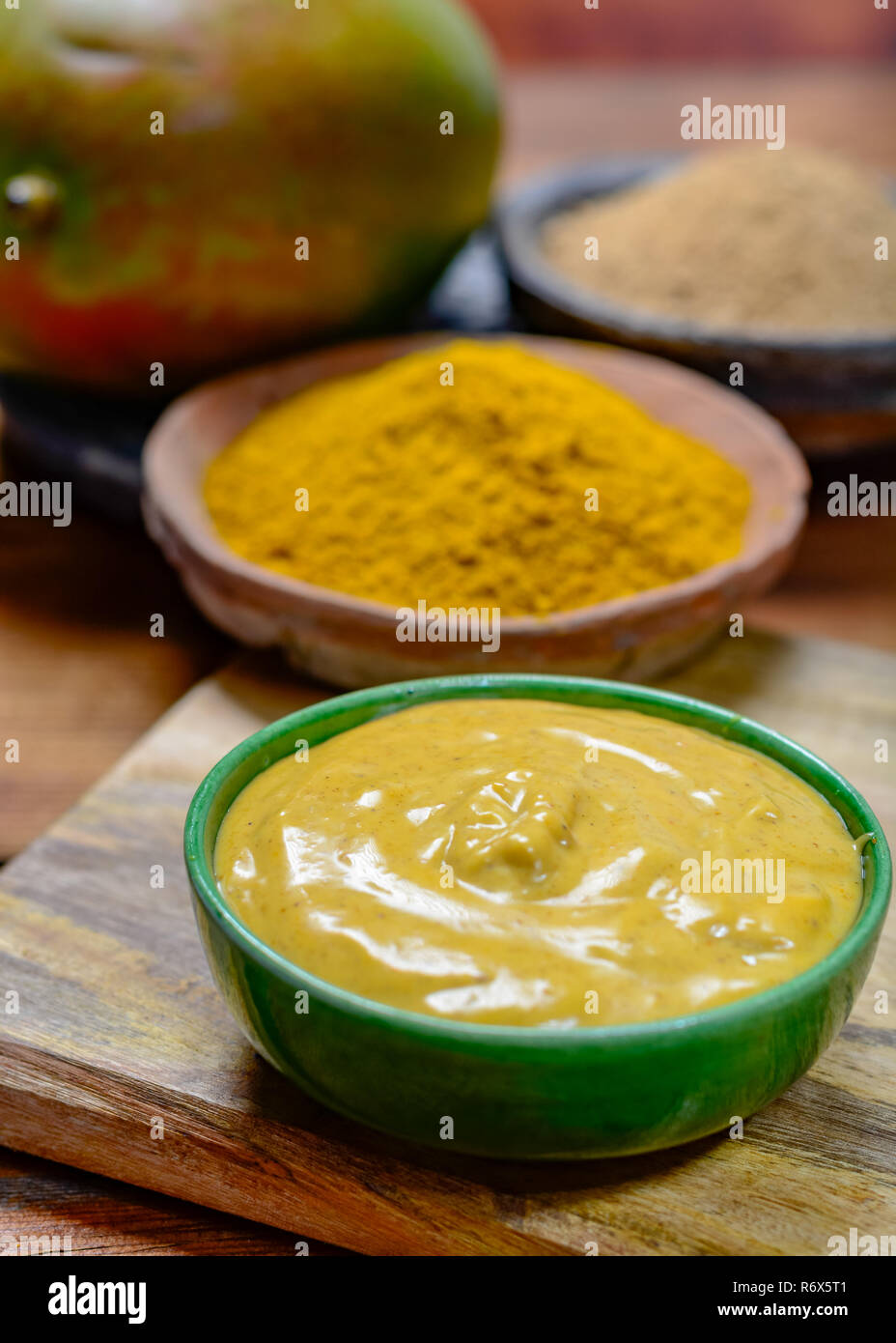 Tasty mango-curry sauce in small bowl ready to eat and bowls with mango and curry powder close- up Stock Photo