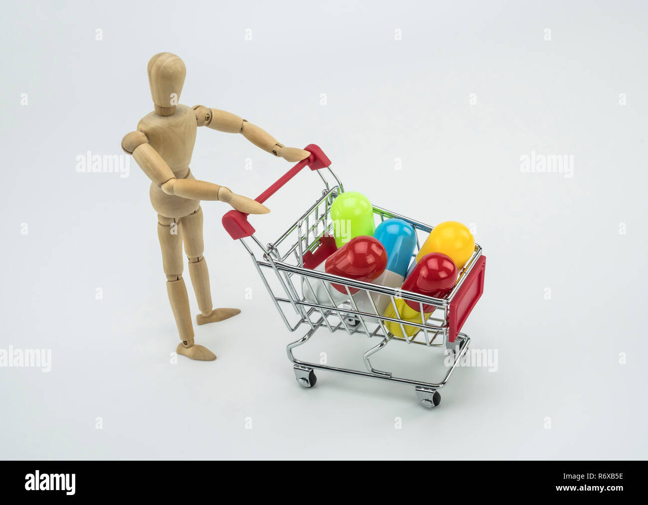 Wooden dummy carries shopping cart with pills, insulated on white background, conceptual image Stock Photo