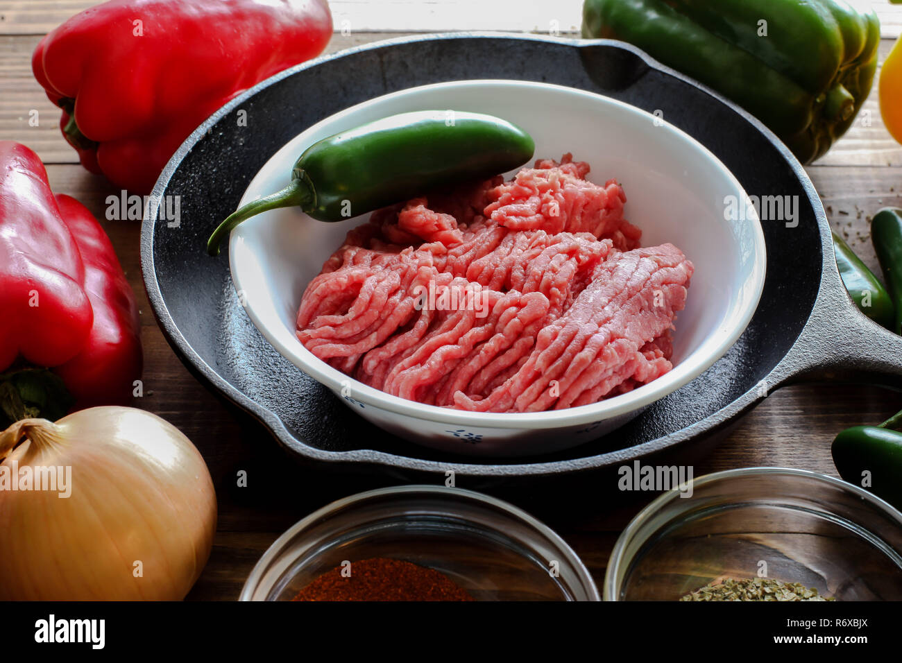 Raw ground beef inside skillet with peppers and other cooking ingredience around with wooden background side view Stock Photo