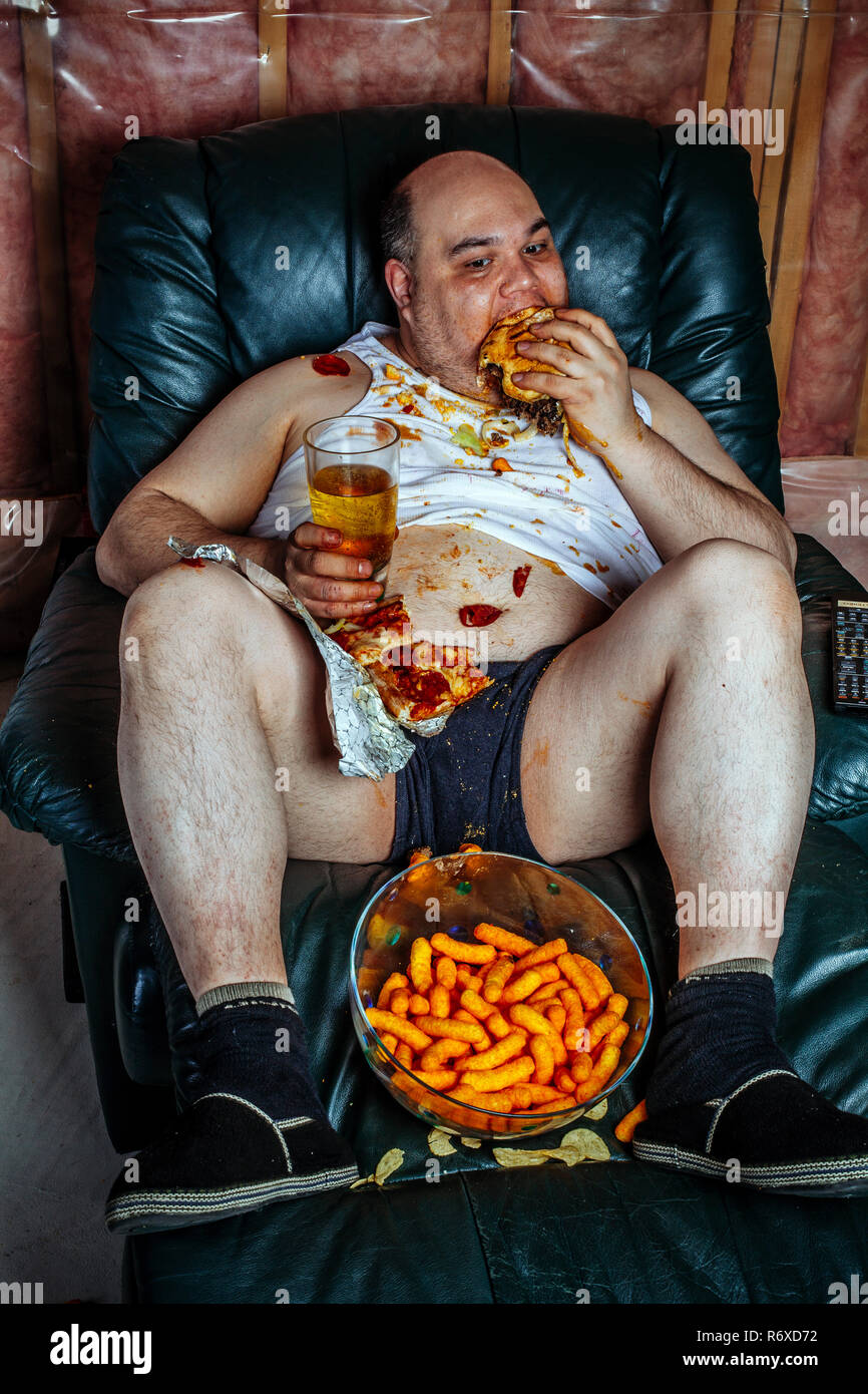Overweight man eating and watching TV Stock Photo
