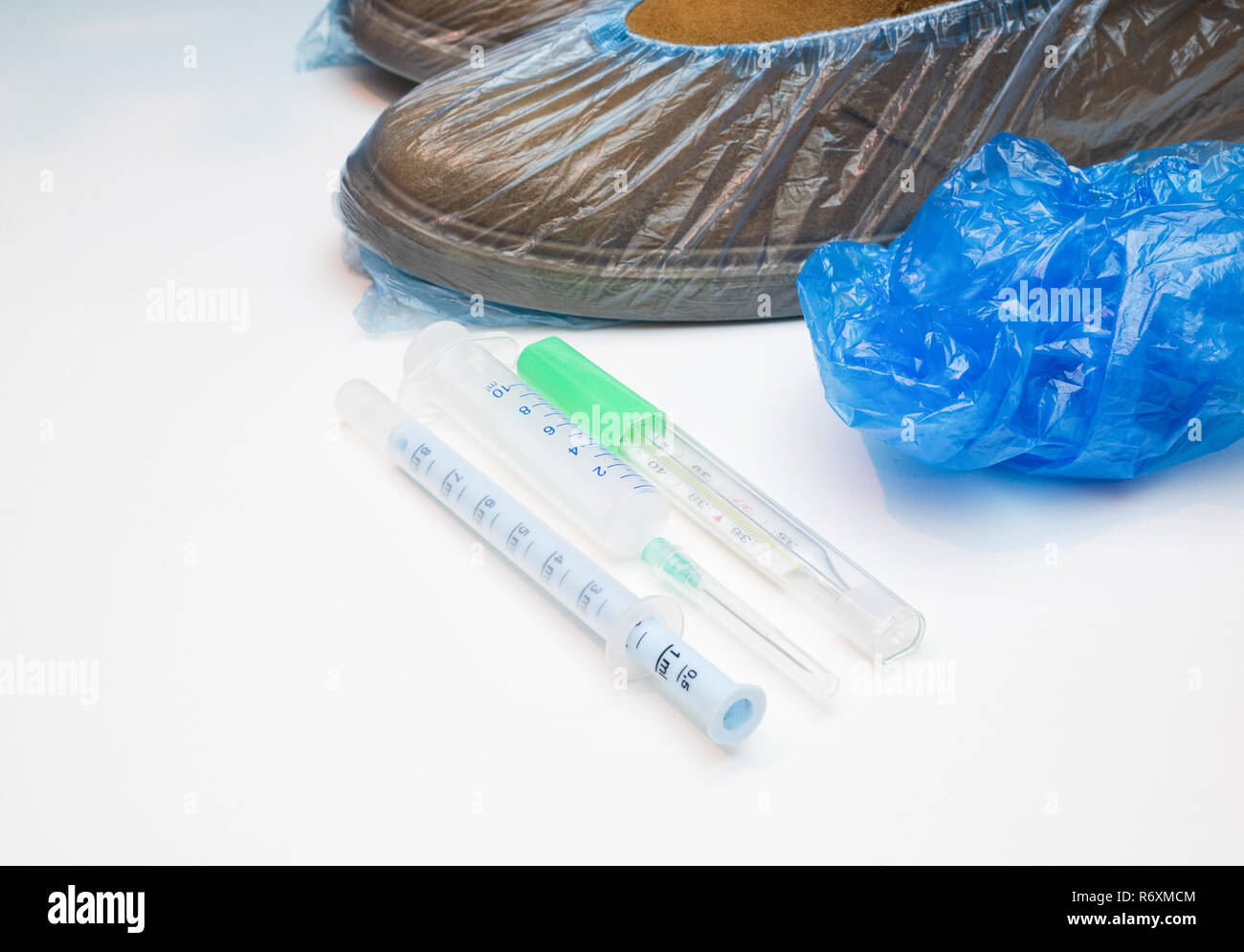 mans shoes in anti dust coves and set of must have medical equipment for patient visiting at hospital - syringe, liquid syrup drug dispenser, thermome Stock Photo