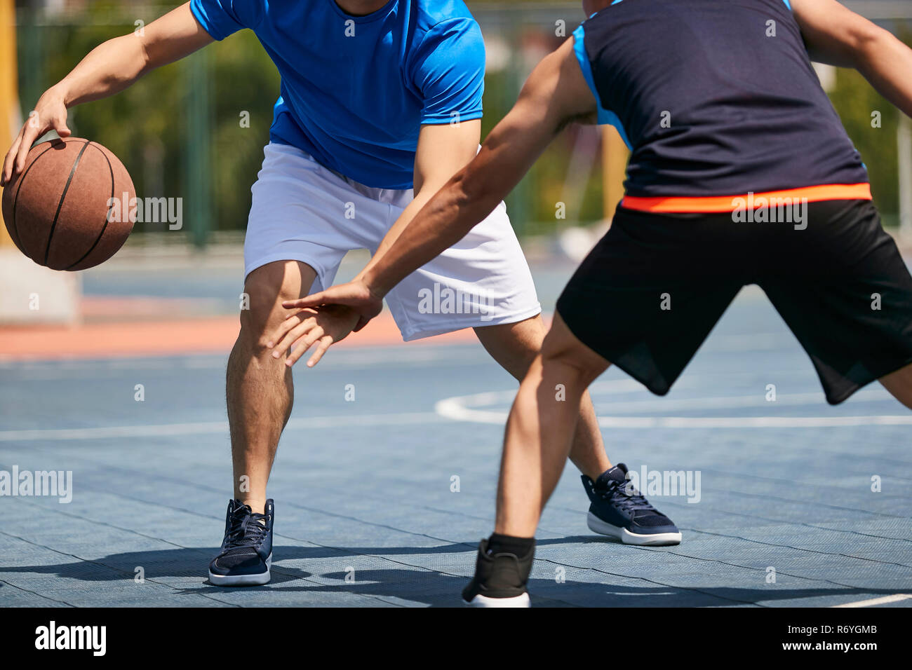 young asian adults playing basketball under the sun on outdoor court. Stock Photo