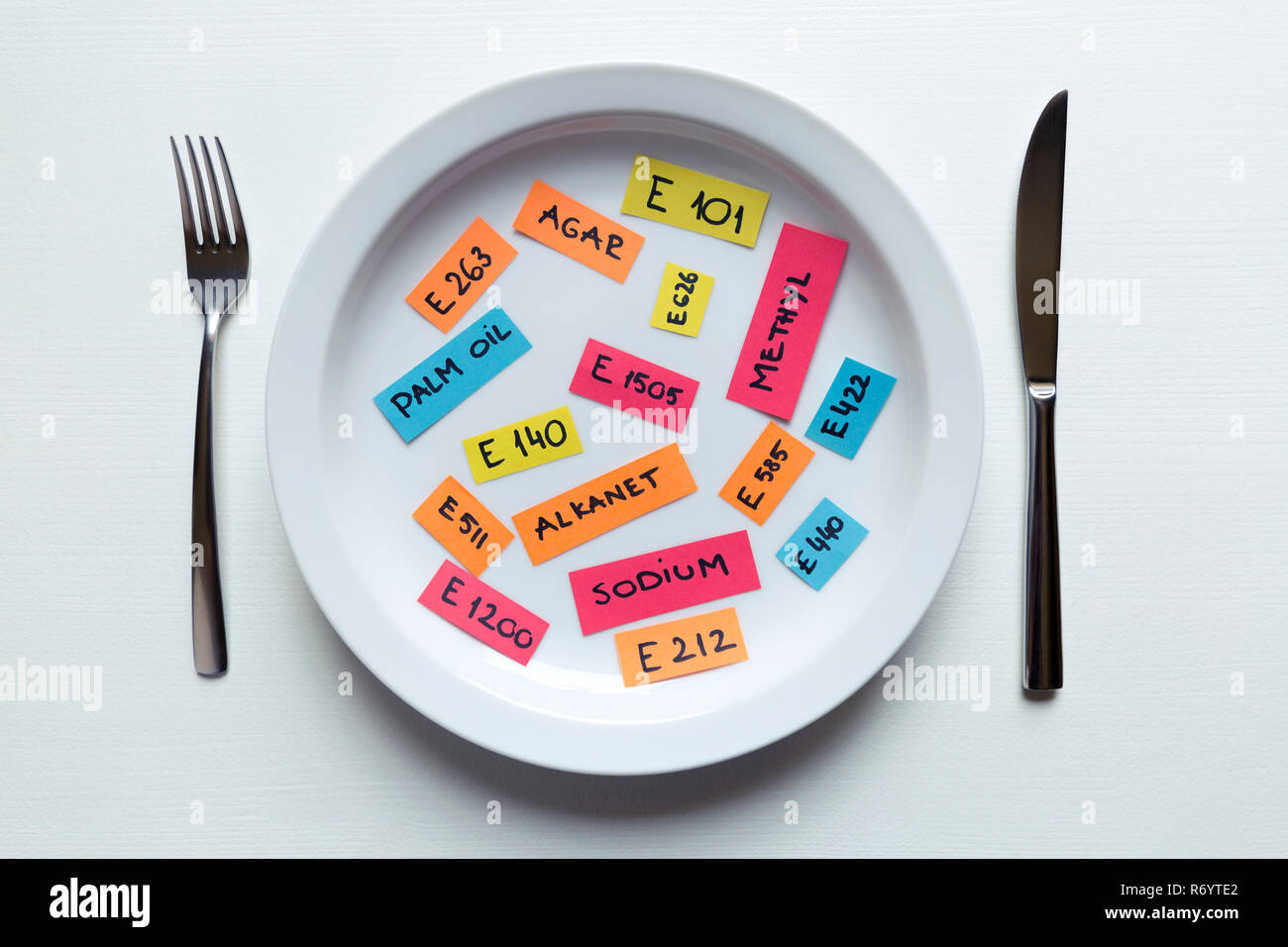 Colorful paper notes naming food additives on plate with fork and knife, food additive and unhealthy food concept. Stock Photo