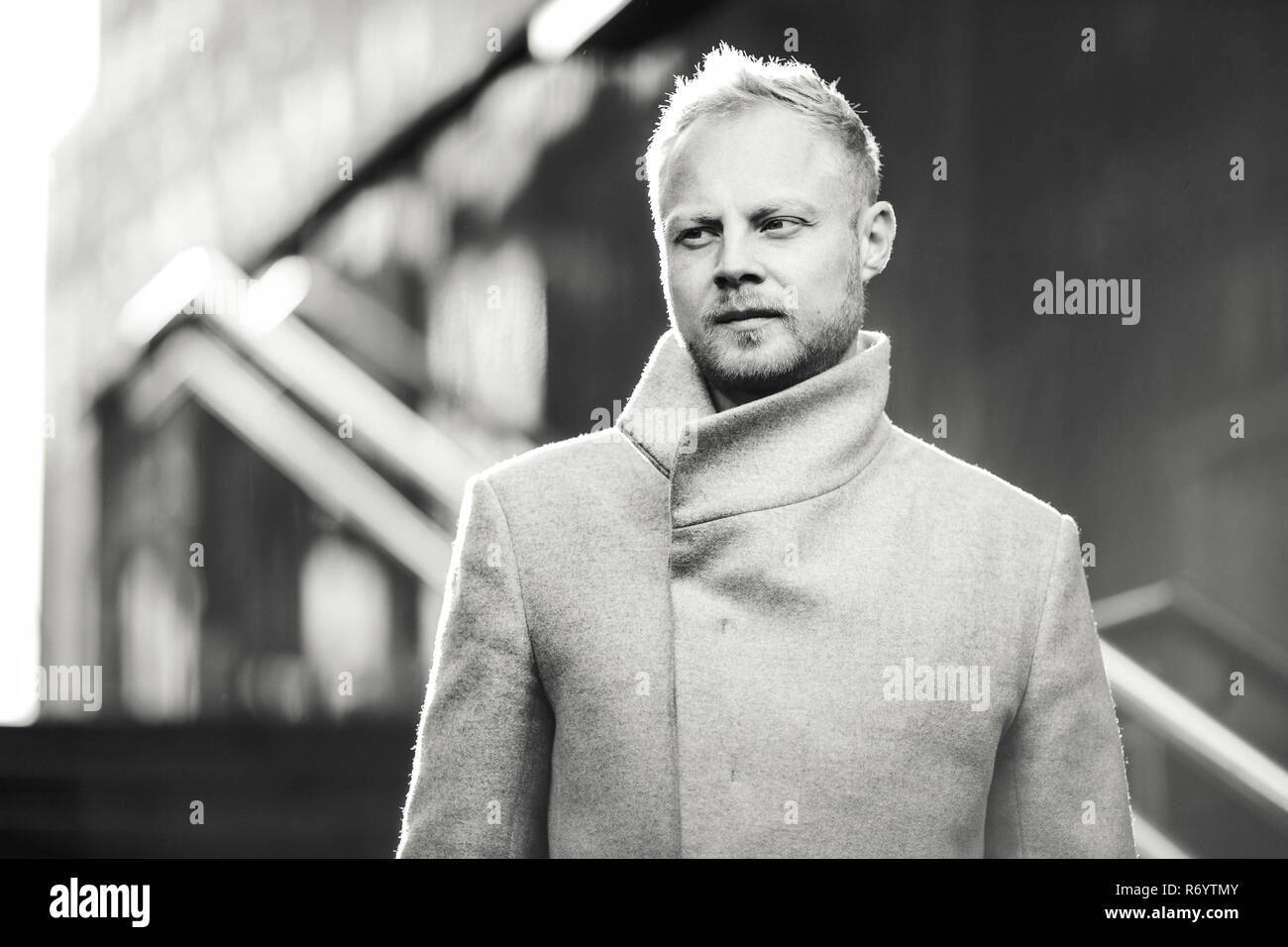 Black and white image of serious man in coat on street, defocused background. Stock Photo