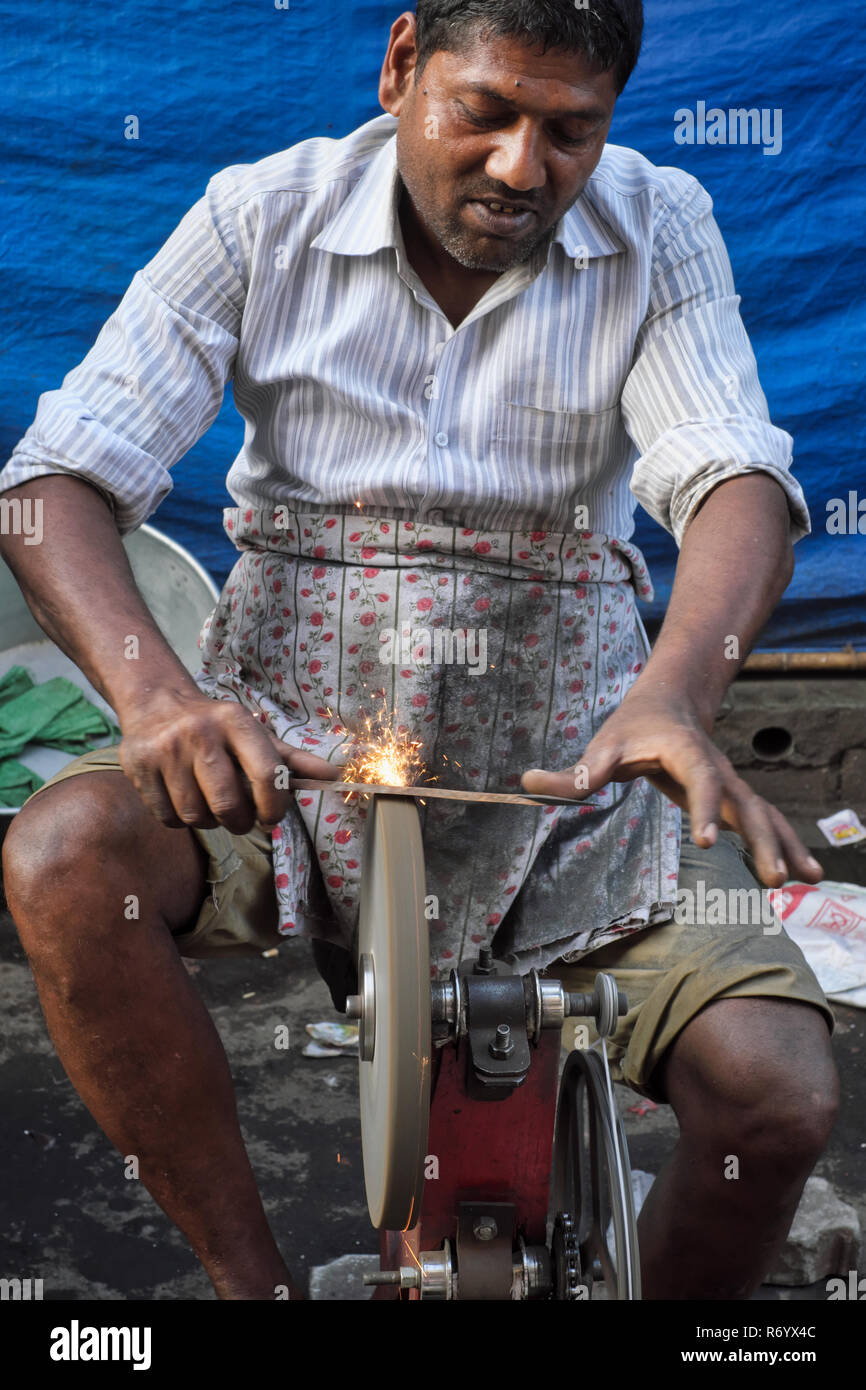 A knife sharpener at work using a whetstone or sharpening wheel propelled via the pedals of a bicycle-like mechanism; Mumbai, India Stock Photo