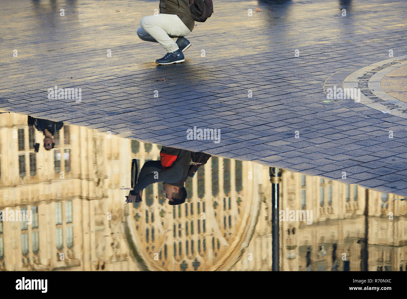 London UK. 7th December 2018. UK Weather. Tourists opposite the Houses of Parliament, seen reflected in a puddle left by heavy morning rains. Credit: Kevin J. Frost/Alamy Live News Stock Photo