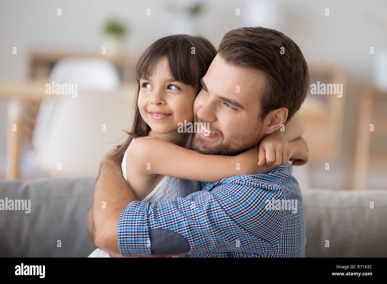 Father and daughter embracing sitting on couch looking at camera Stock Photo