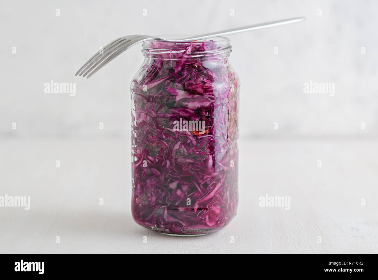Glass jar of palatable purple fermented cabbage with fork standing on white background Stock Photo