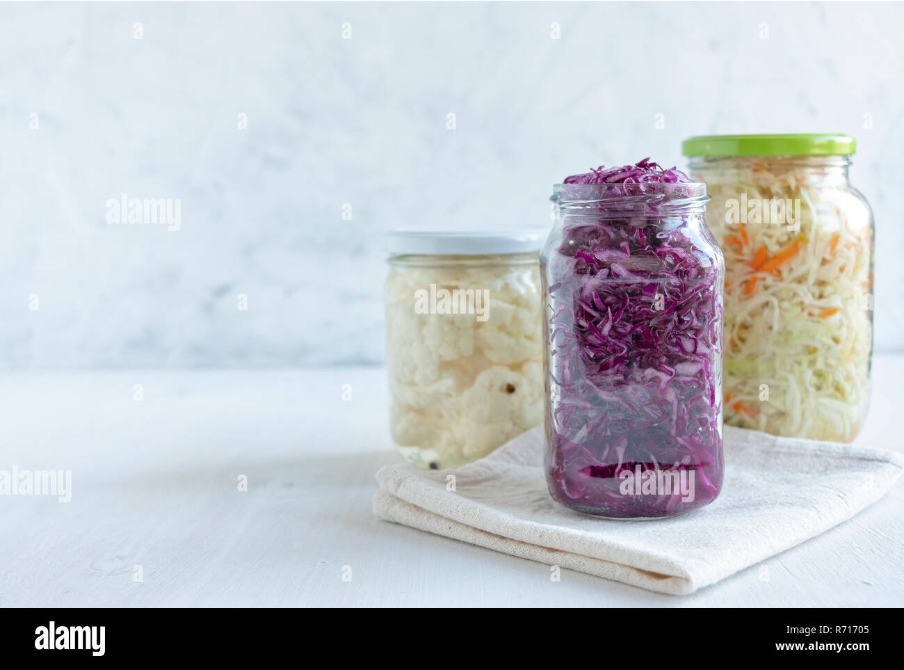 Three jars with various delectable fermented vegetables standing near napkin on white background Stock Photo