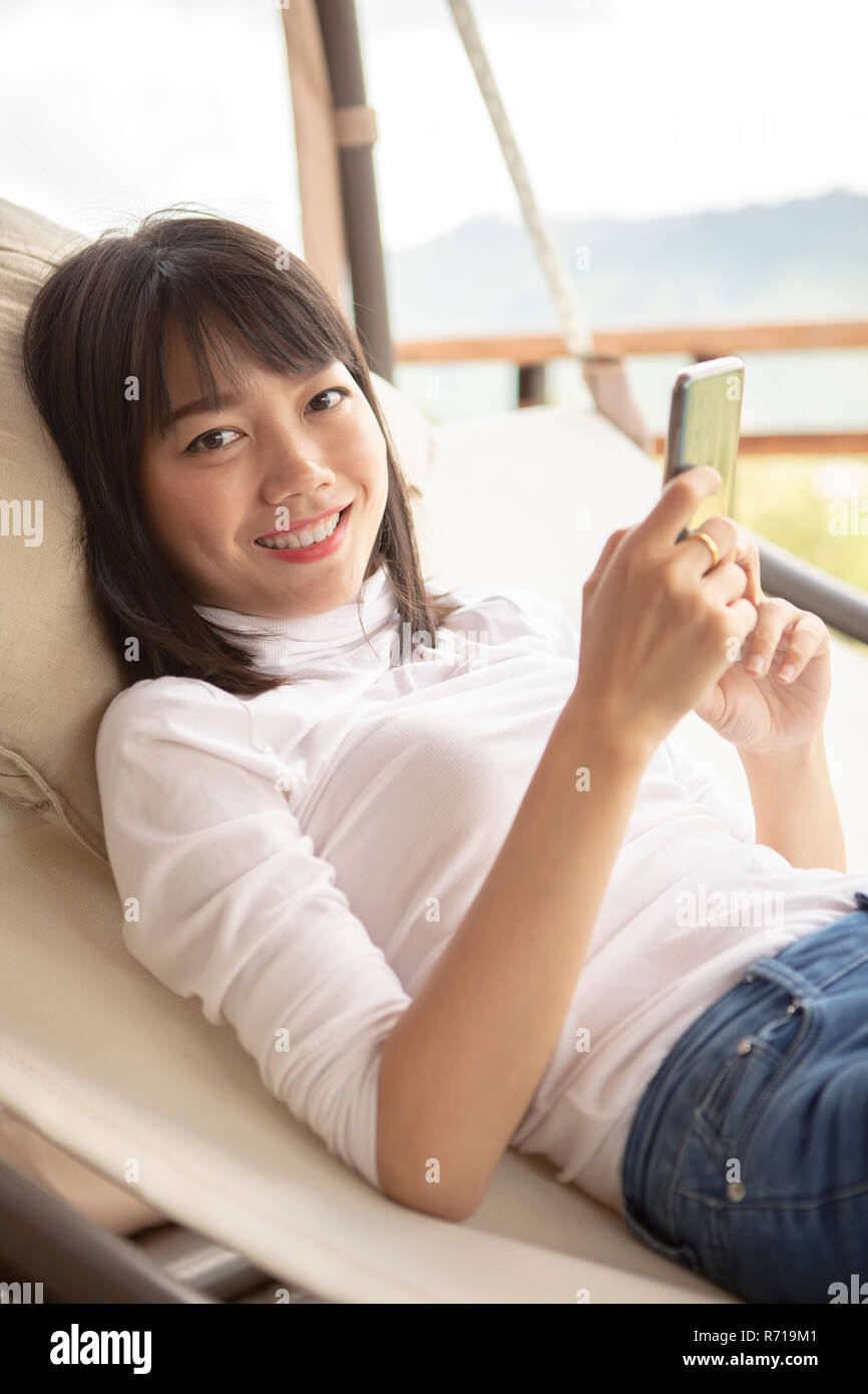 beautiful asian younger woman relaxing  holding smartphone  on cradle Stock Photo