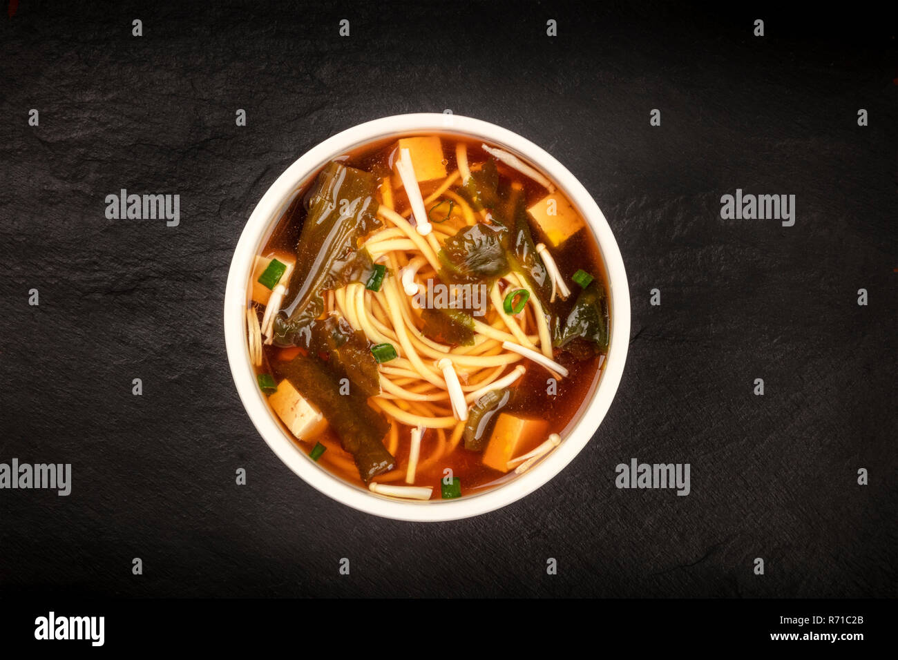 A Photo Of A Bowl Of Miso Soup With Tofu Scallions Noodles Wakame And Enoki Mushrooms Shot From The Top On A Black Background With A Place For Te Stock Photo