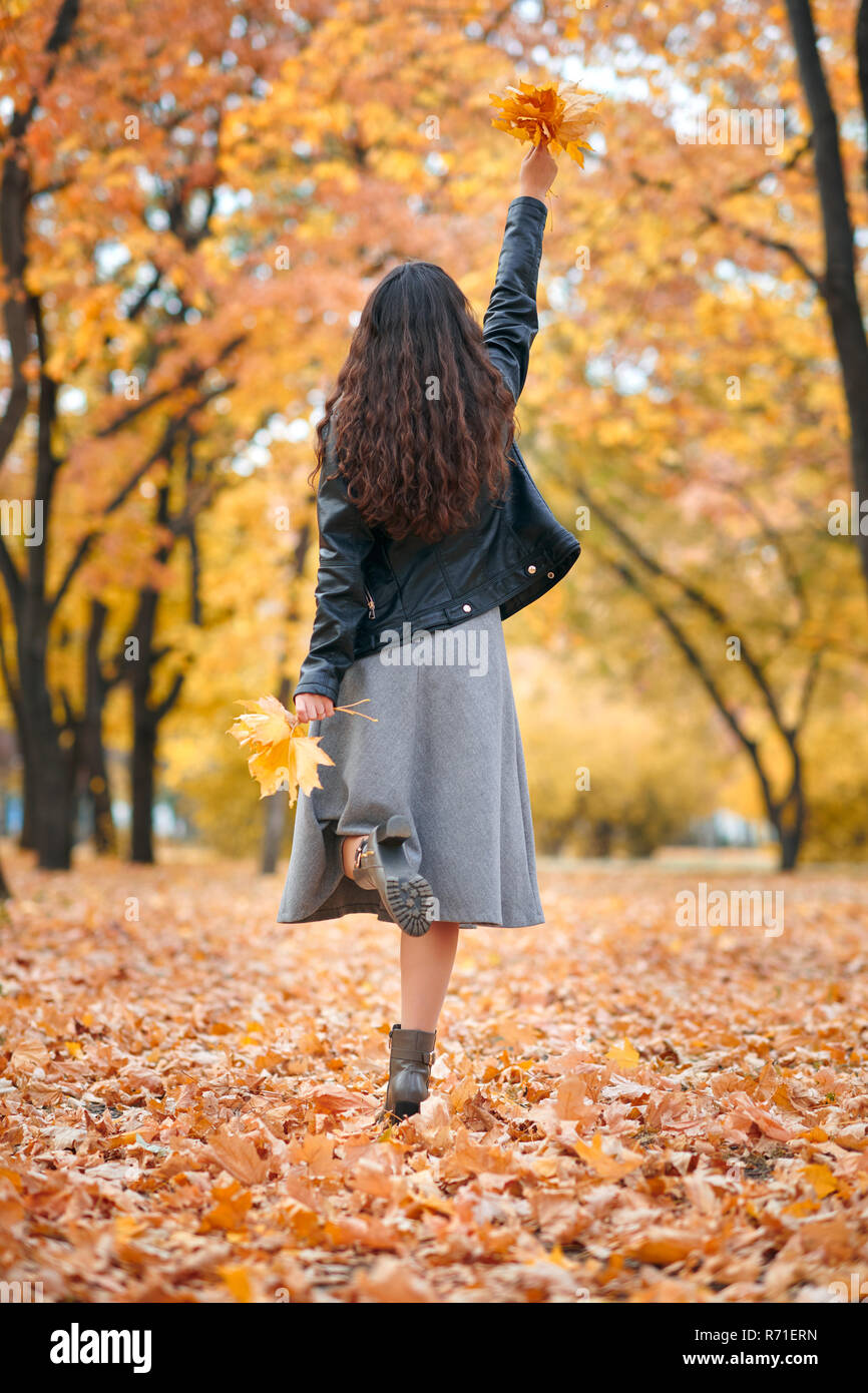 Pretty woman posing with bunch of maple's leaves in autumn park. Beautiful landscape at fall season. Stock Photo