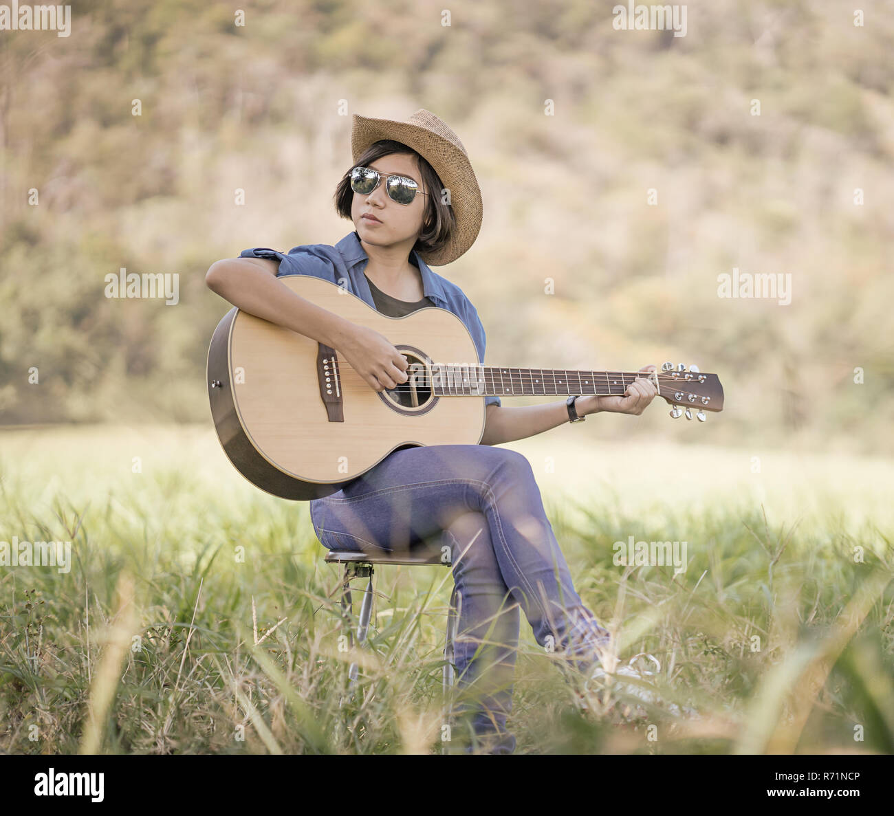 Women short hair wear hat and sunglasses sit playing guitar in grass field  Stock Photo - Alamy