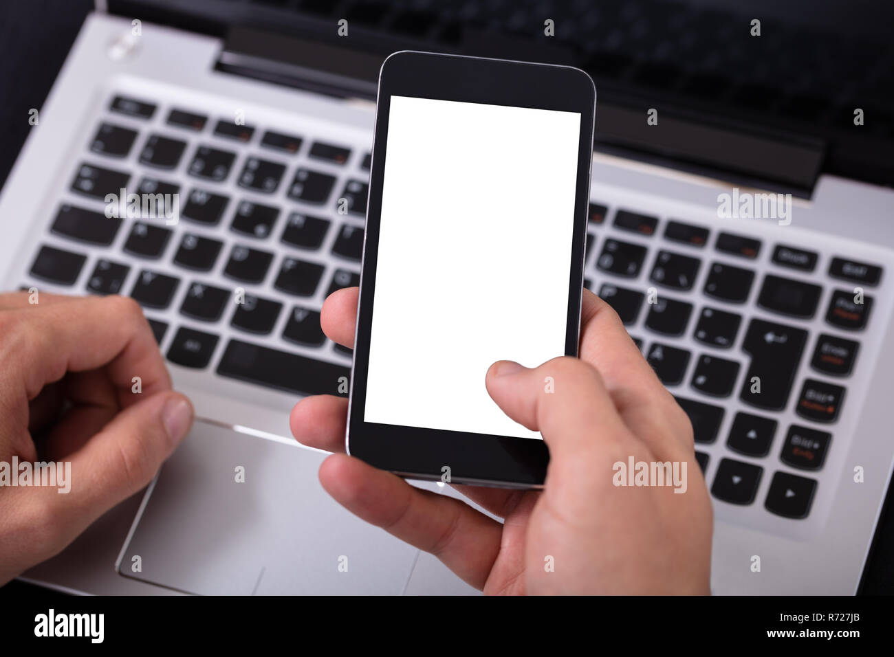 Man Using Mobile Phone With Blank White Screen Over Laptop Stock Photo