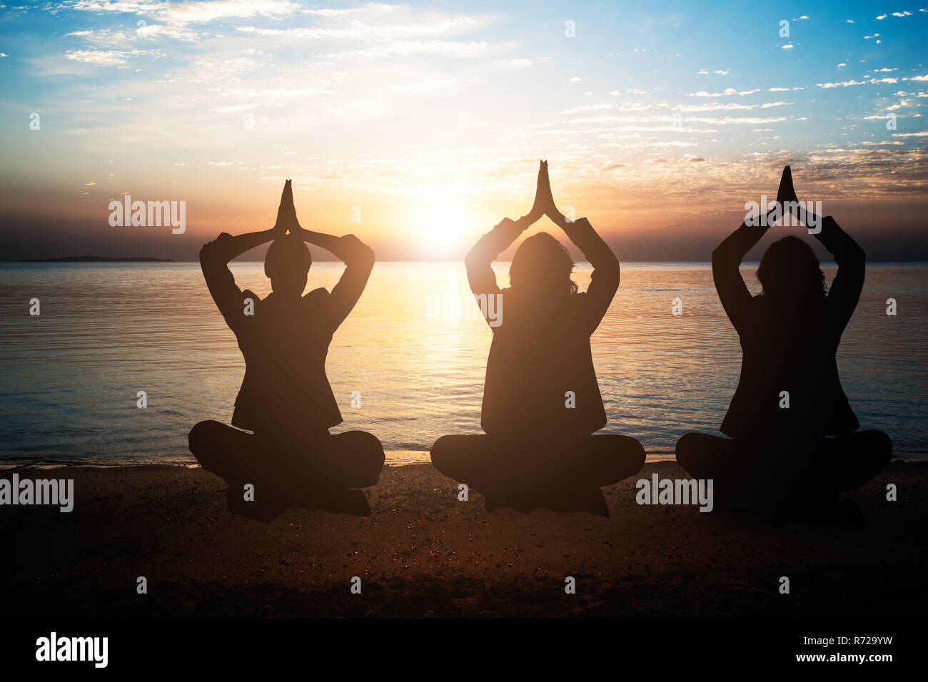 Silhouette Of People Meditating At Beach During Sunset Stock Photo