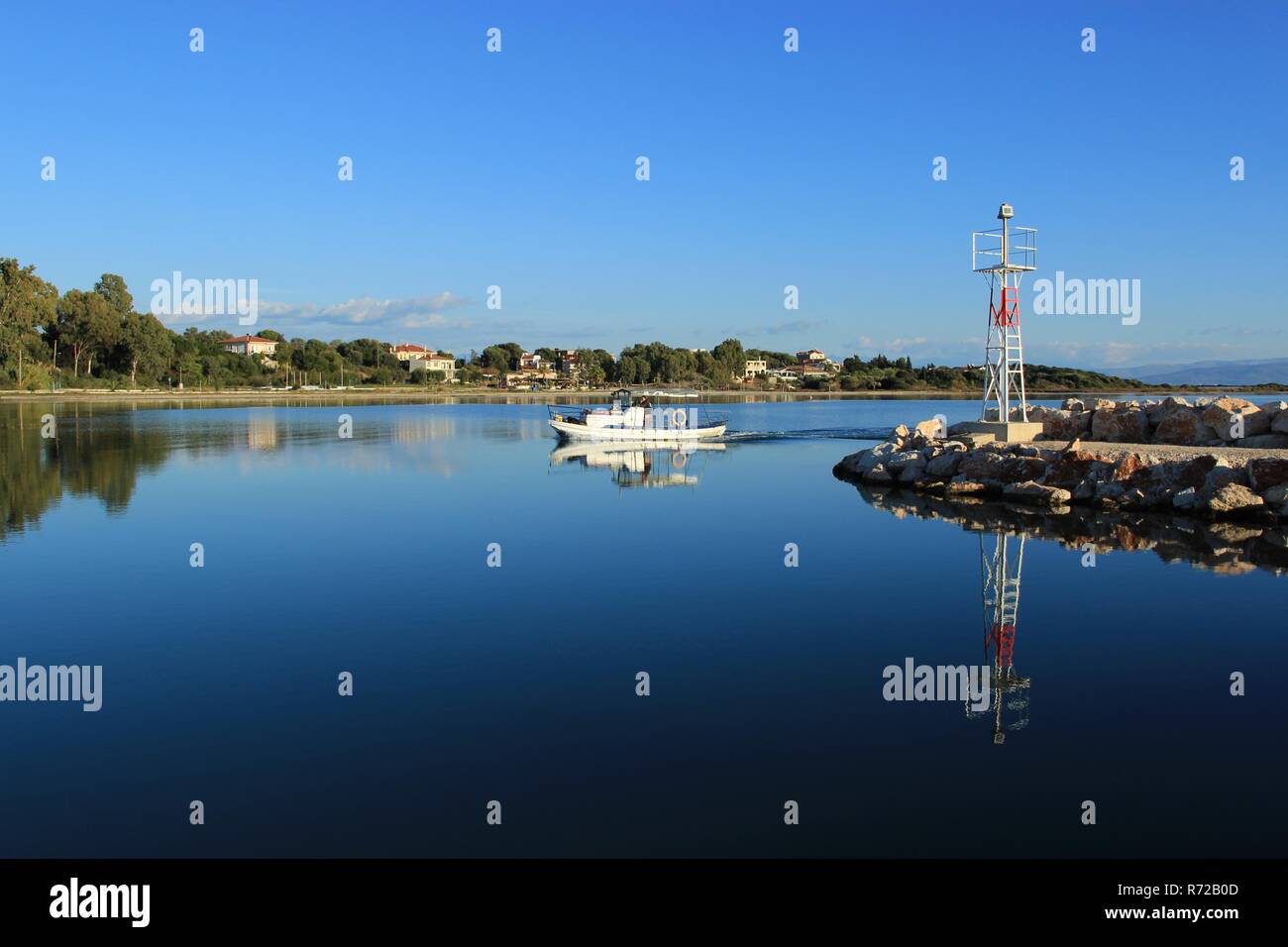 Small white wooden fishing boat entering a port of Koronisia village in Ambracian gulf in Greece near a beacon at summer Stock Photo