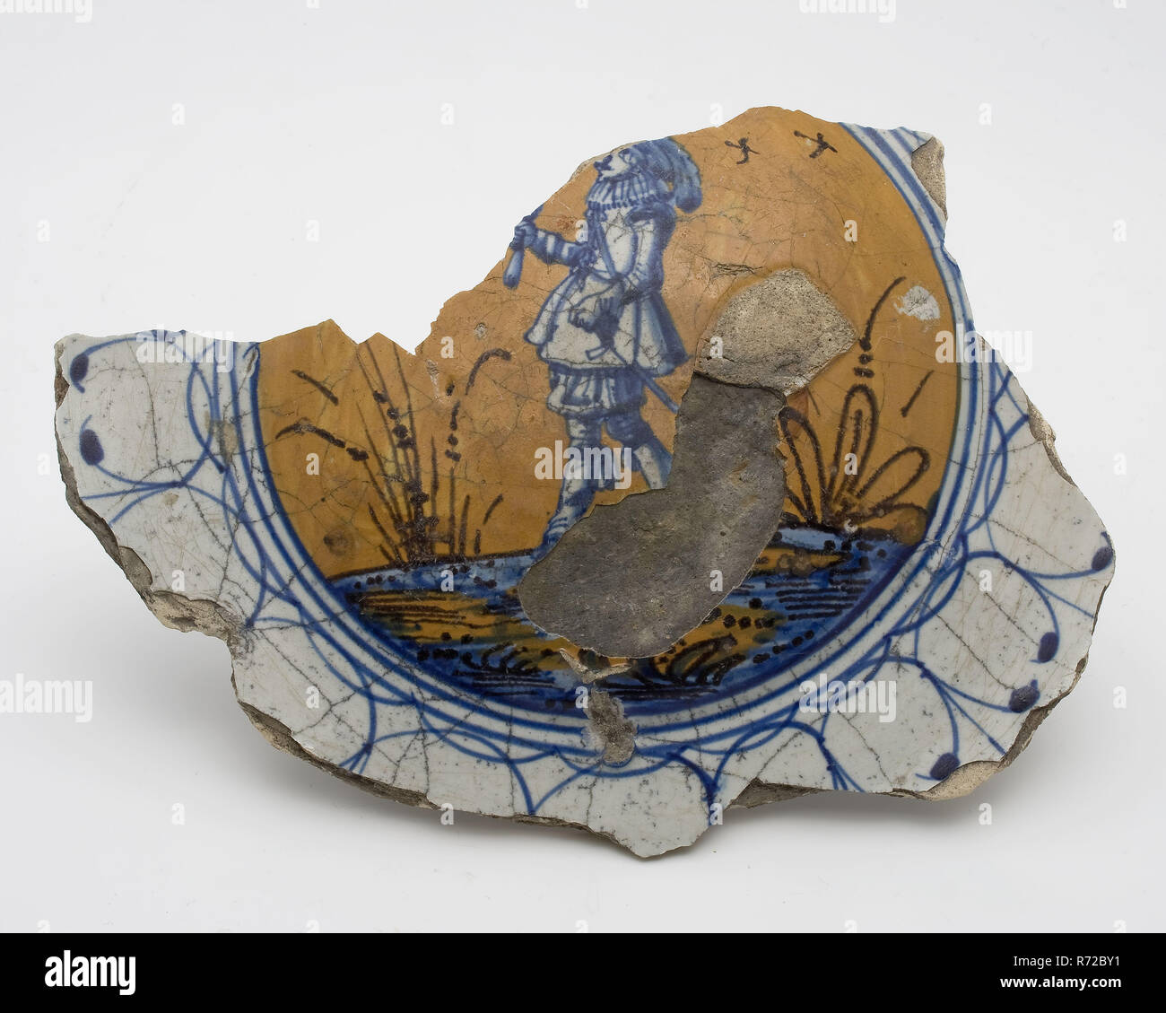 Majolica dish fragment, man in rich clothing, polychrome, pancake dish, dish crockery holder soil find ceramic pottery glaze tin glaze lead glaze, majolica shaped baked painted fried Fragment of pancake dish. Fried on prunes Yellow shard scraped earthenware. Depicted is man or soldier in rich clothes on an orange and blue ground. Serious baking fault in the middle but no misbaksel: many scratches in the glaze indicate domestic use archeology Rotterdam decorate interior serve serve food Italy archaeological find in the soil Rotterdam 1941. Stock Photo
