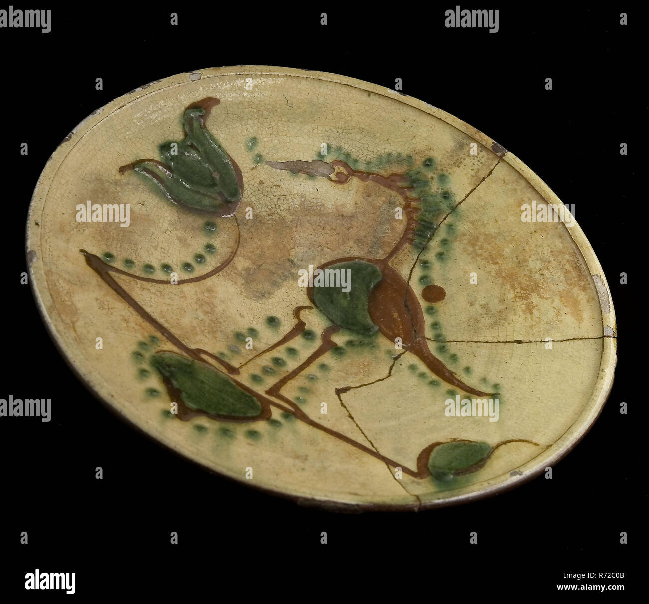 Dish on stand, red earthenware with bird and flower on yellow ground, plate crockery holder soil find ceramic earthenware glaze lead glaze clay, hand-turned decorated glazed fried lemonade Deep saucer on stand ring Upright sidewall without shoulder Red shard only glazed at the top Decorated in sludge technique Decoration consists of bird long legs in red and green to the left of it tulip or floral pattern archeology indigenous pottery import food serve serve table decorate Stock Photo