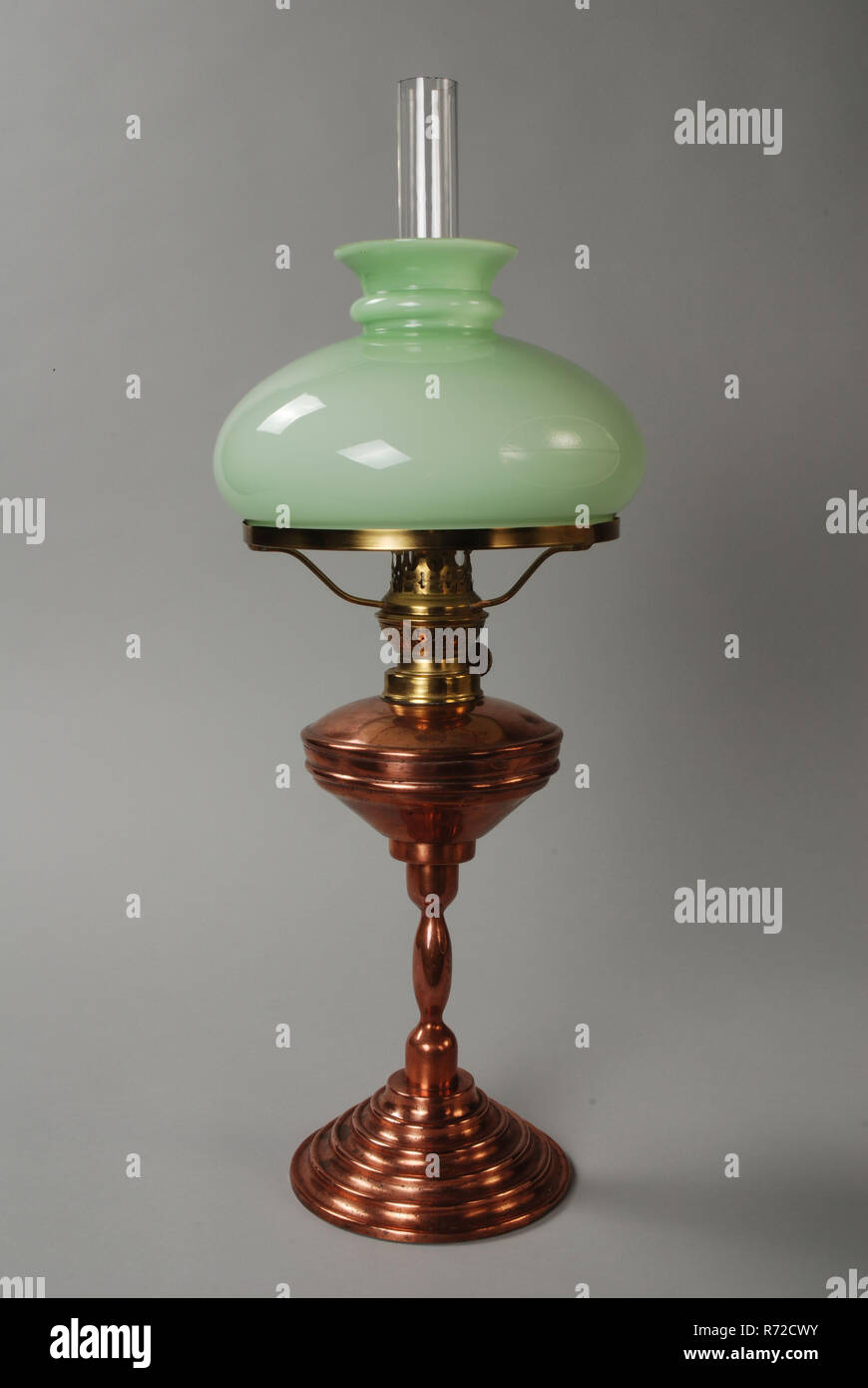Christoffel Vennix, Copper oil lamp, oil lamp lamp illuminant copper glass metal textile cotton, Oil lamp or kerosene lamp. Table lamp on high foot Red copper column on foot with ascending steps. Conical tank with burner and frame of the cap in yellow copper. Hood of green glass and milk glass, on the turning wheel of the burner: KOSMOS BRENNER lighting evening night petroleum illuminate interior craft coppersmith Rotterdam migration Brabant Noord-Brabant Stock Photo
