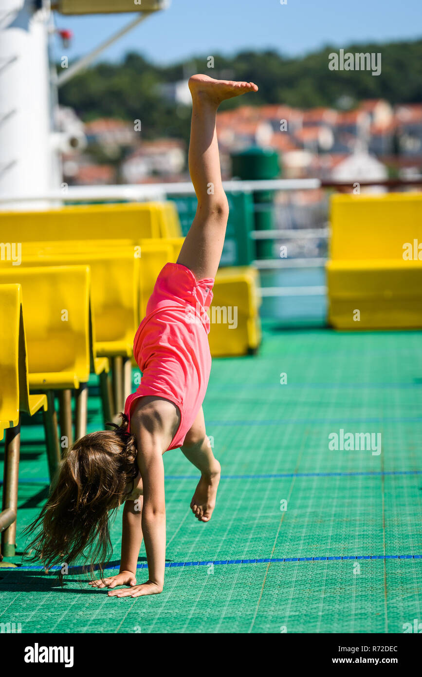 Girl doing cartwheels on Croatian ferryboat in Mali Losinj. Little girl is activly doing cartwheels on vacation. Concept of active children, fitness a Stock Photo