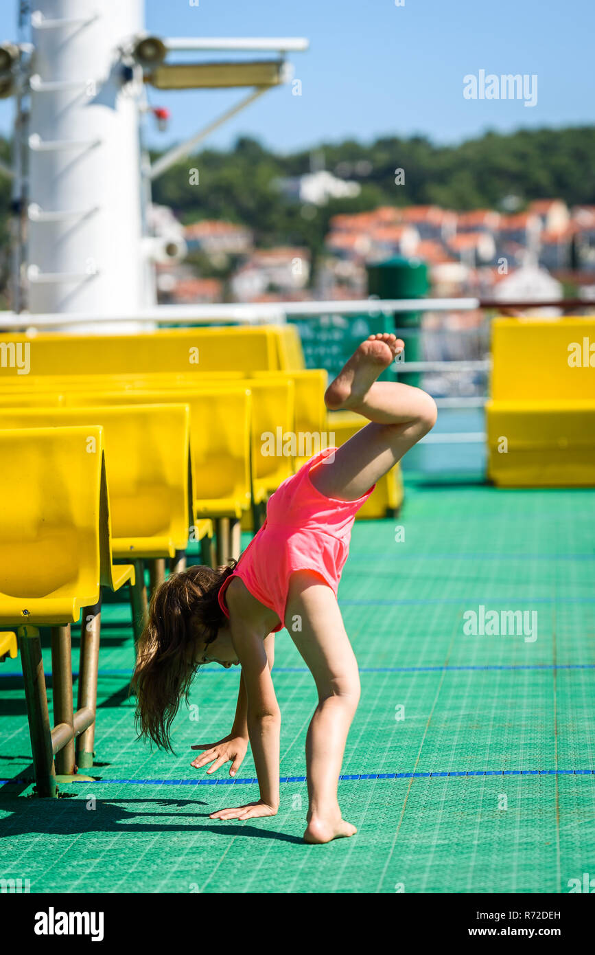 Girl doing cartwheels on Croatian ferryboat in Mali Losinj. Little girl is activly doing cartwheels on vacation. Concept of active children, fitness a Stock Photo