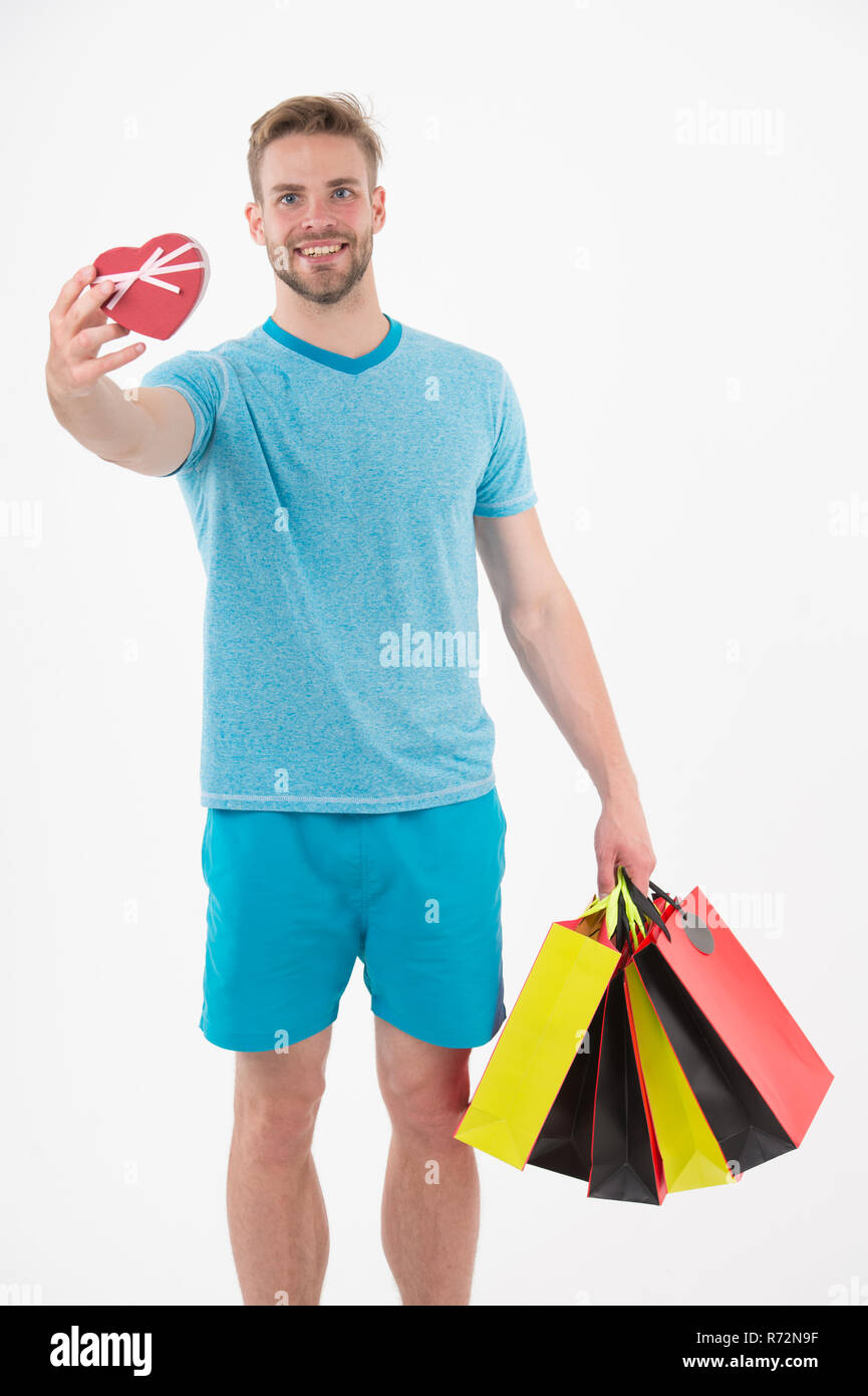 Happy man with heart and shopping bags isolated on white. Macho smile with  paper box and bags. Fashion shopper in blue tshirt and shorts. Valentines  day preparation. Shopping sale and black friday