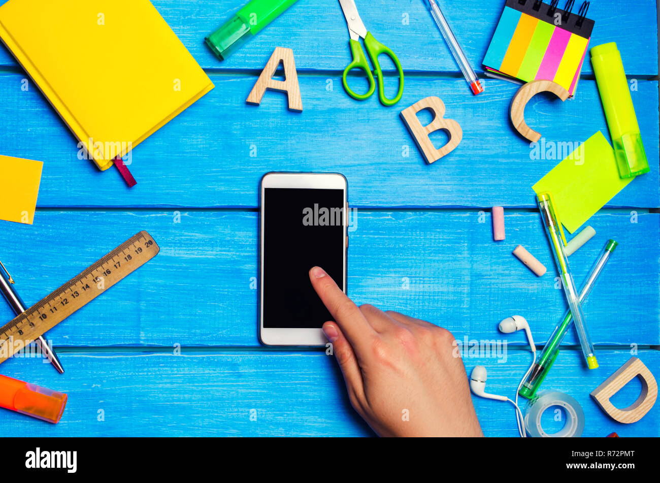 student points to the phone, digital diary or e-book,reluctance to learn, school supplies on a blue background. educational application. telephone add Stock Photo