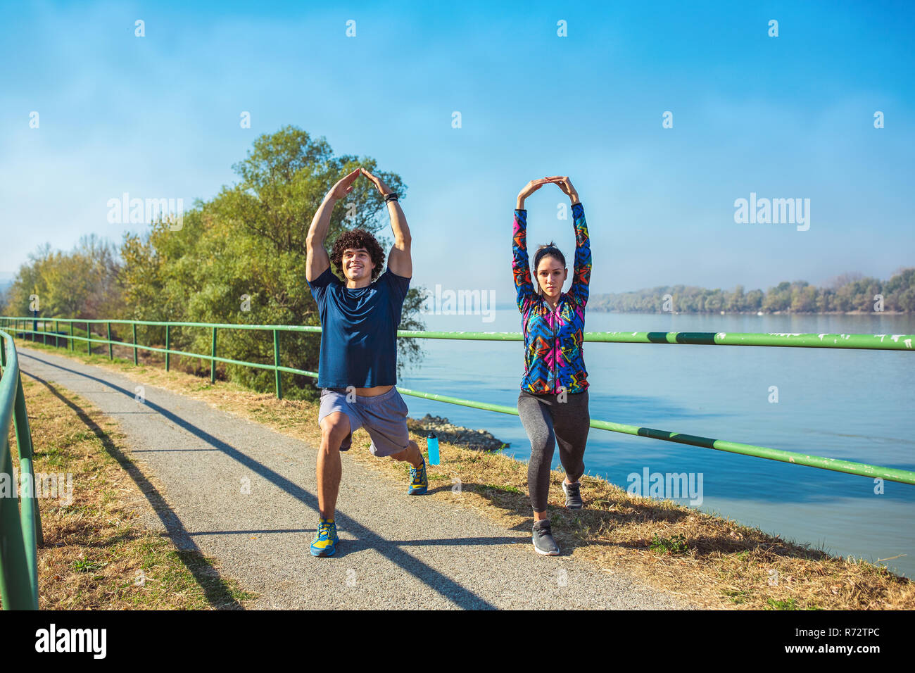 young fitness man and woman stretching in the park. Young couple warming up in morning. Stock Photo