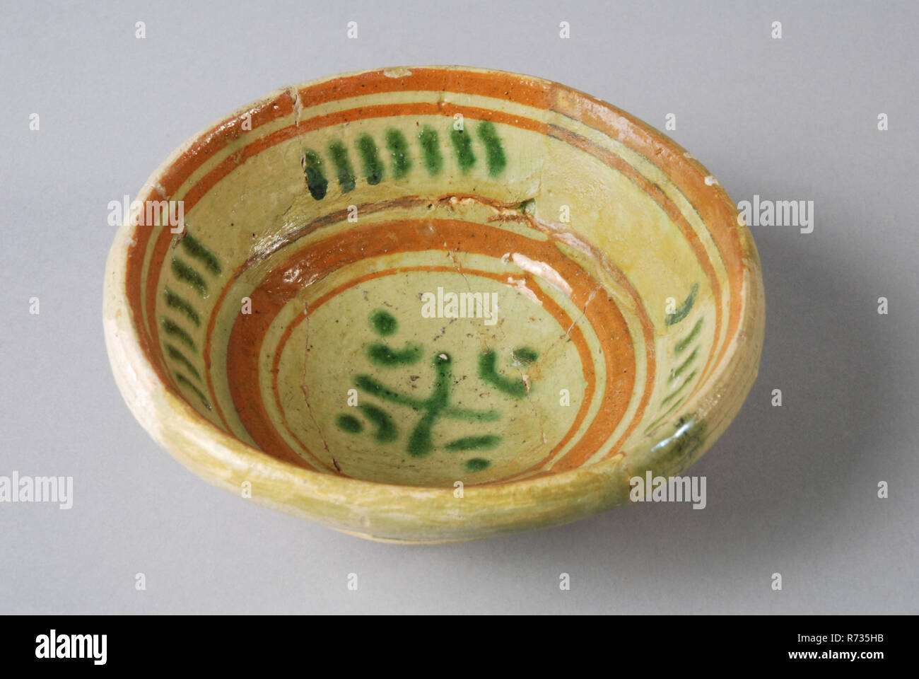 Pottery comes on small stand, gray shard, with circles and stripes in silt decoration, bowl bowl tableware holder soil find ceramic earthenware glaze lead glaze, hand turned decorated glazed decorated fried ring lead Lead glaze. White shard. Yellow and green silt decoration in circles between which green dot and stripe sludge trim. Deep bowl on small standing surface Sharply raised sidewall. Shoulder on the transition from mirror to bowl edge Restoration is repainted but in form poorly executed archeology underground pit Rotterdam City Triangle Groenendaal indigenous pottery import food servin Stock Photo