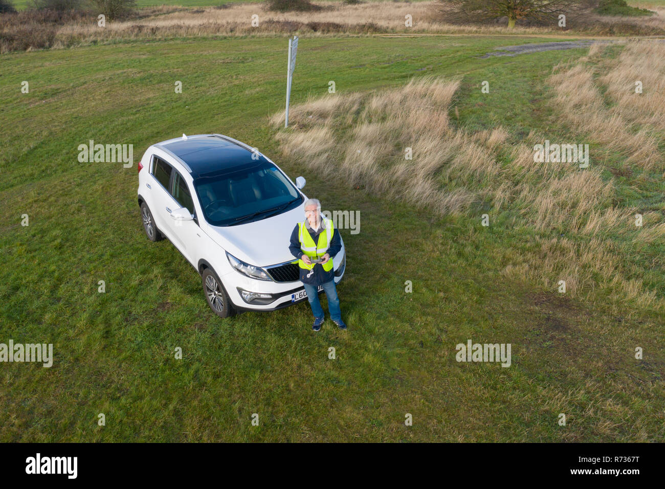 Drone SUAV pilot with remote controller in hand and wearing a hi viz jacket flying in a large field. Stock Photo