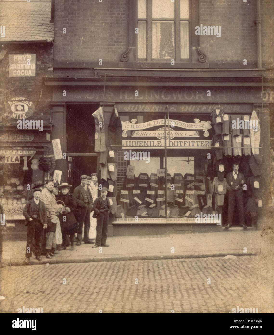 Edwardian photograph of J.A.S(James) Illingworth Juvenile Outfitters, Tailor and Clothier. 18 Attercliffe Road, Sheffield,South Yorkshire, England, U.K. Assistants / staff and customers from the grocery store next door have also posed for the photograph whilst the owner of the tailors maintains a dignified and humorless pose. Circa 1905. Stock Photo